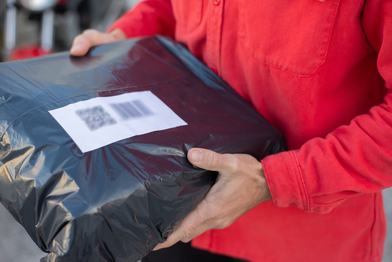 Close-up of hands holding a black parcel with a barcode label while wearing a red shirt.
